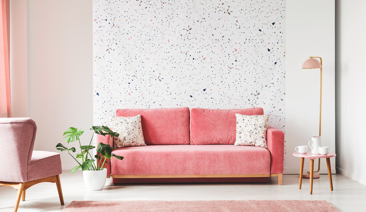Real photo of a pink, velvet sofa, plant, coffee table with pot and cups on a lastrico wall a living room interior